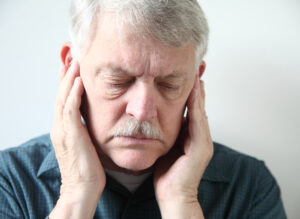 older man holds both hands to his upper jaw near the ears